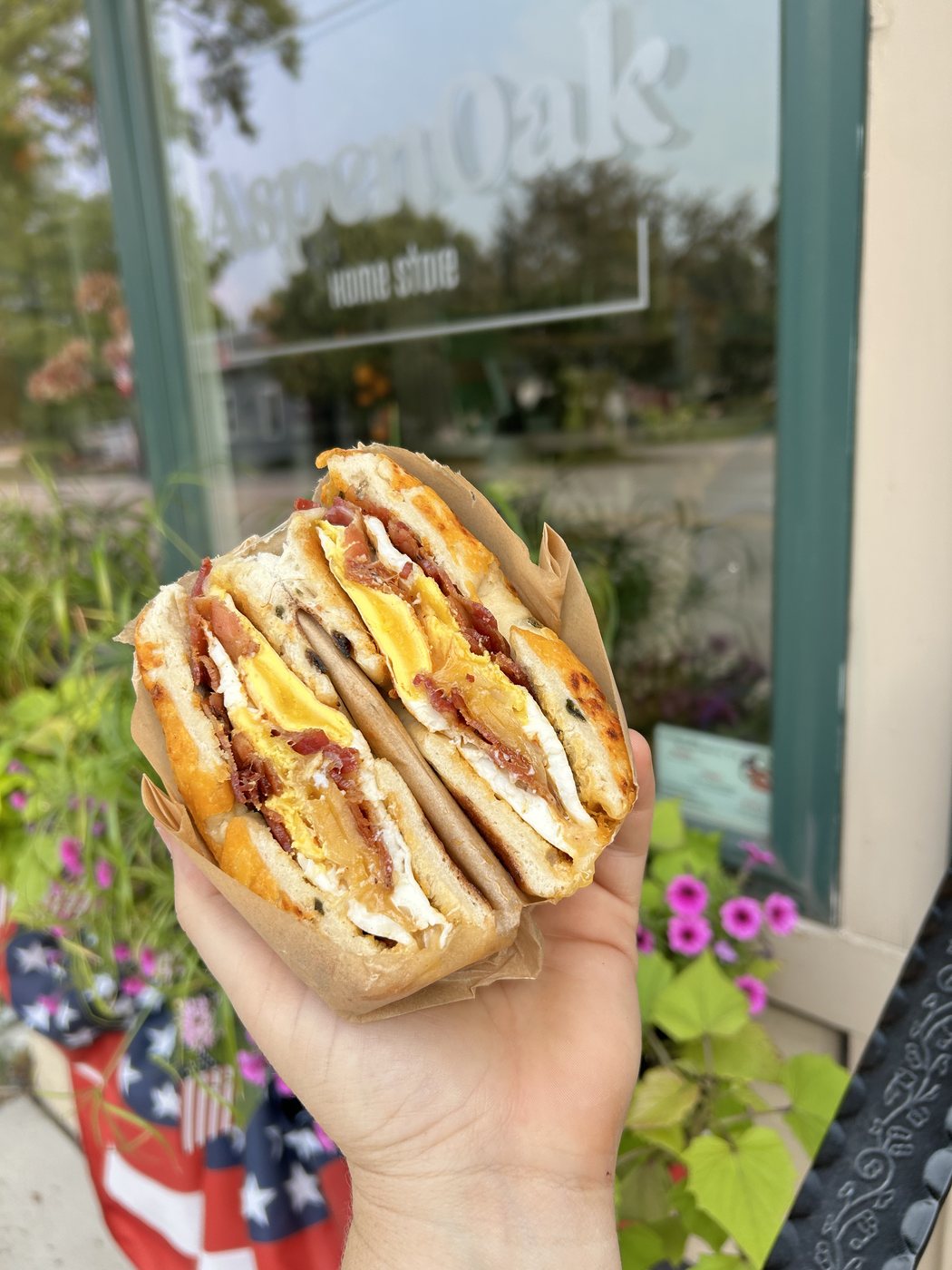 A loaded AspenOak bagel sandwich held up outside the storefront