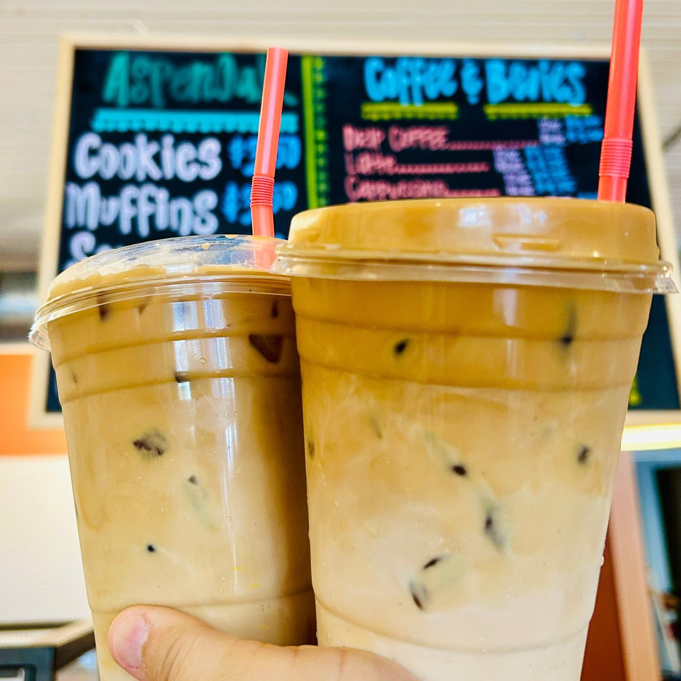 Two iced lattes in front of the AspenOak coffee board